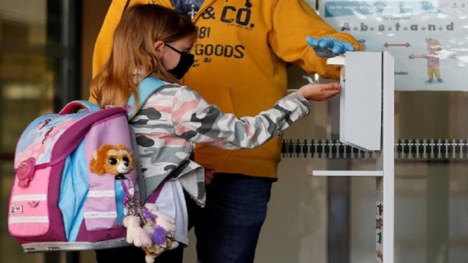 Seorang anak mengenakan masker sedang membersihkan tangan dengan cairan antiseptik saat hendak masuk sekolah (REUTERS,Leonhard Foeger)