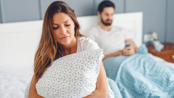 jealous-unsatisfied-girlfriend-holding-pillow-sitting-bed-while-her-husband-using-smart-phone-reading-writing-message-selective-focus-woman_232070-6548