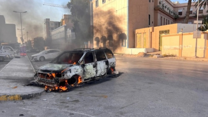 Sebuah mobil terbakar di jalan selama bentrokan terjadi di Tripoli.