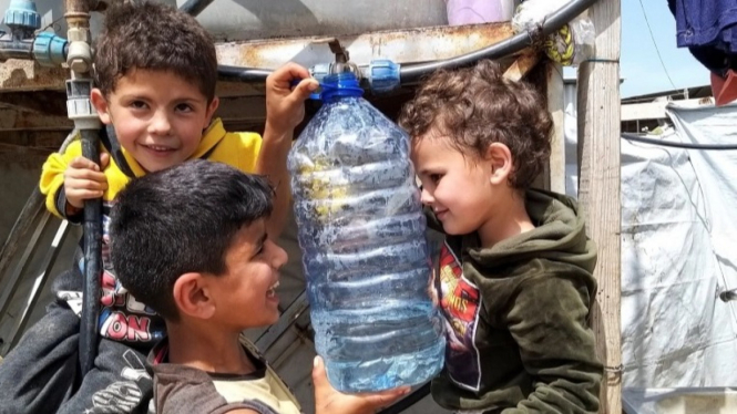 Pengungsi Suriah di Lebanon memegang botol air.