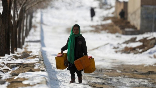 Seorang anak Afghanistan bawa wadah air kosong di wilayah bersalju.