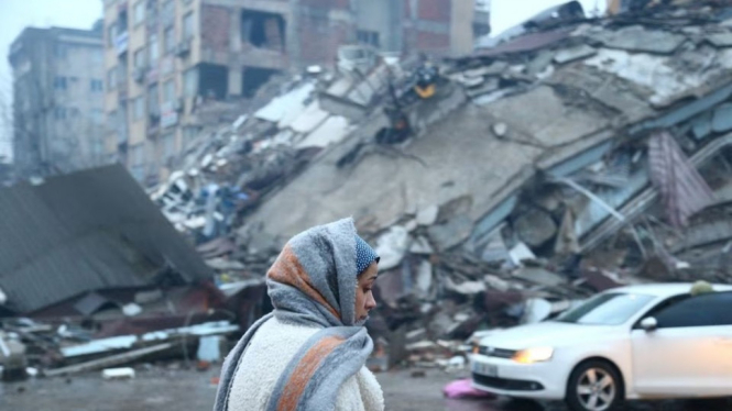 Seorang wanita berjalan di depan bangunan roboh akibat gempa Turki.