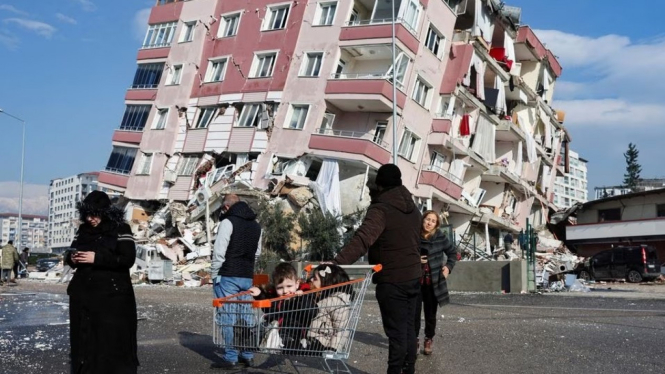 Warga berdiri di depan bangunan roboh akibat gempa Turki.