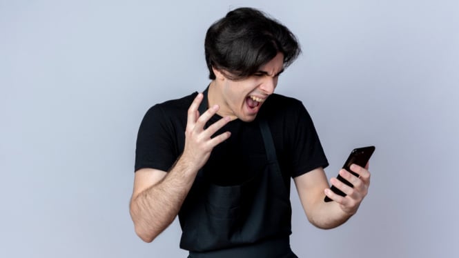 Remaja sedang menggunakan smartphone dengan ekspresi kesal