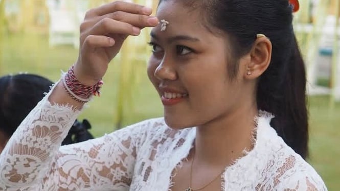 Seorang perempuan Hindu Bali sedang menempelkan bija di keningnya