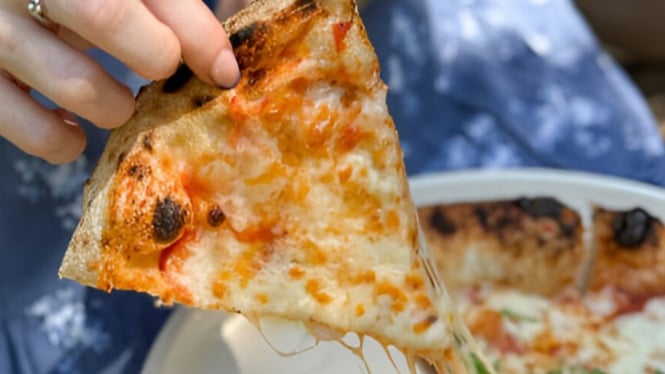 Seorang wanita sedang memegang sepotong pizza Margherita