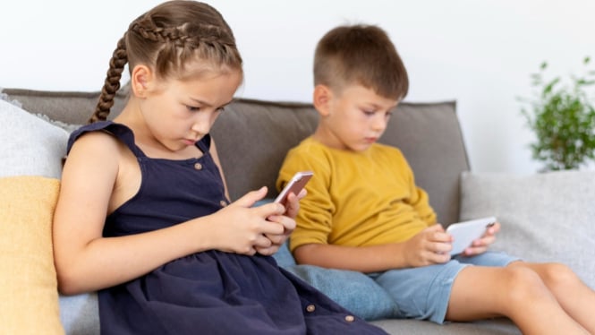 Dua orang anak yang sedang asyik bermain gadget
