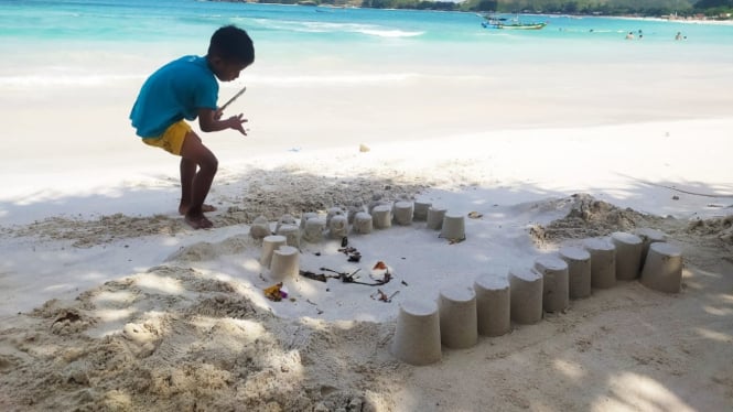 Seorang anak sedang bermain pasir di pantai Tanjung Aan