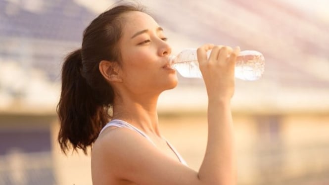 Seorang Wanita yang sedang minum air putih kemasan