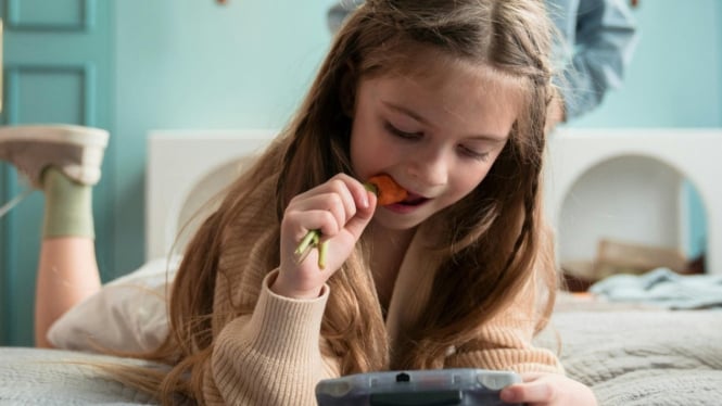 Ilustrasi seorang anak yang makan sambil bermain gadget.