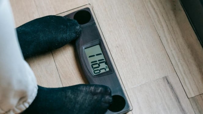 Ilustrasi seseorang yang sedang menimbang badan saat melakukan diet.