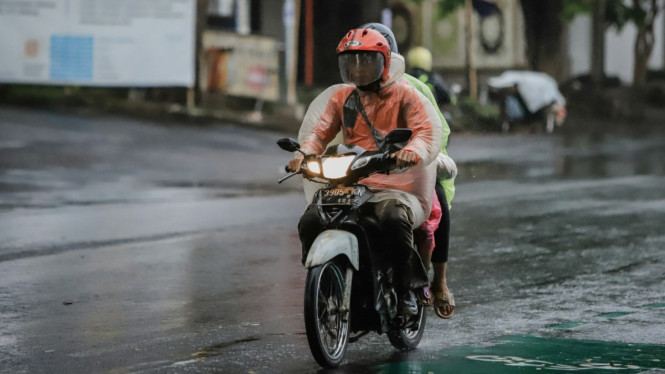 Seorang pria mengendarai motor dengan jas hujan