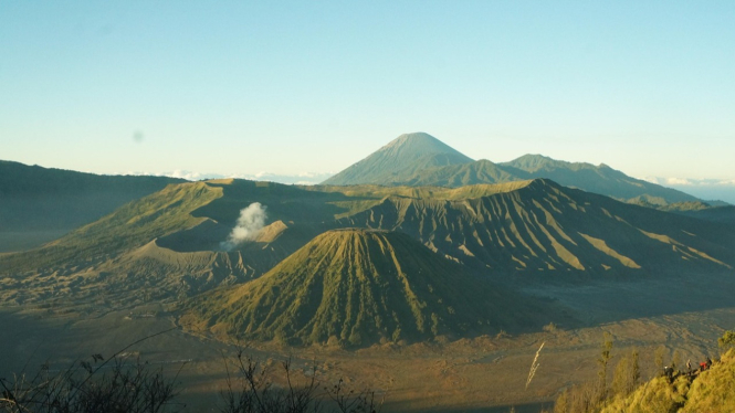 Gunung Bromo mengeluarkan asap sedang diapit oleh gunung lainnya