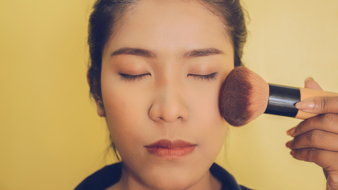 Seorang wanita memakai blush on di area pipi