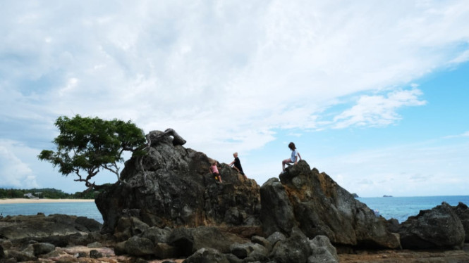 Wisatawan sedang bermain di bebatuan yang ada di pantai