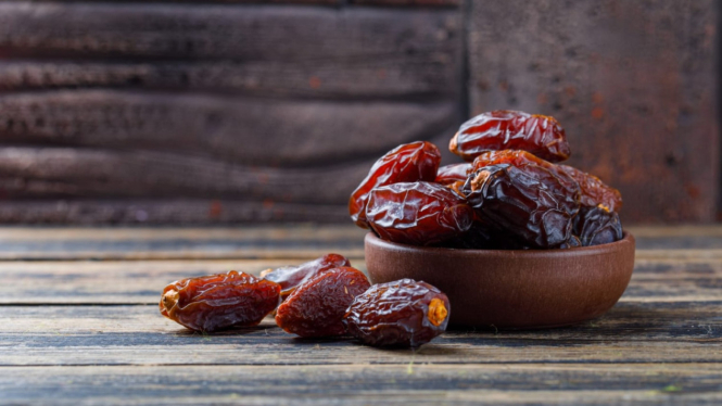 Semangkuk kurma manis dengan latar ubin batu dan kayu