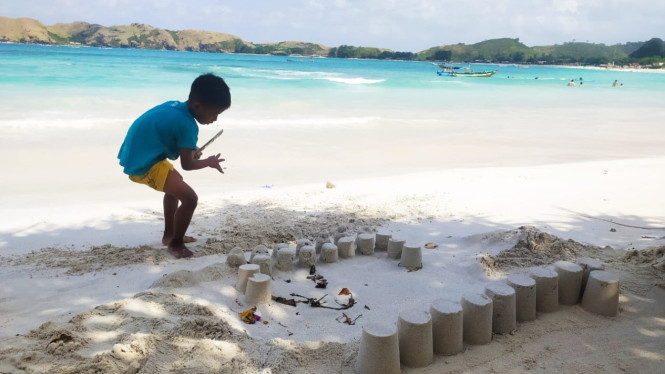 Seorang anak sedang bermain pasir di pantai Tanjung Aan