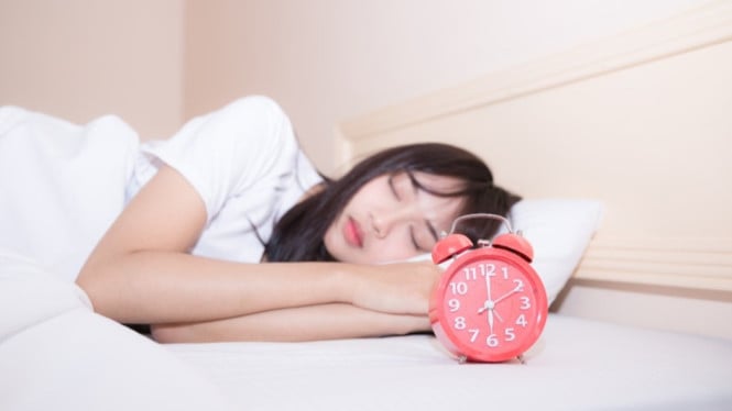 Perempuan tidur dengan jam weker sebagai recovery sleep time.