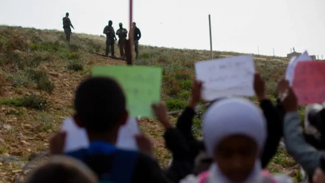 Anak-anak Palestina angkat papan tanda selama protes akses jalan ke sekolah ditutup kawat berduri.