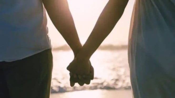 Potret sepasang kekasih gengan tanggan di pantai
