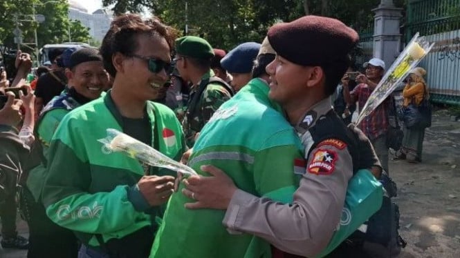 Ojol dan polisi dalam aksi damai beri bunga mawar.