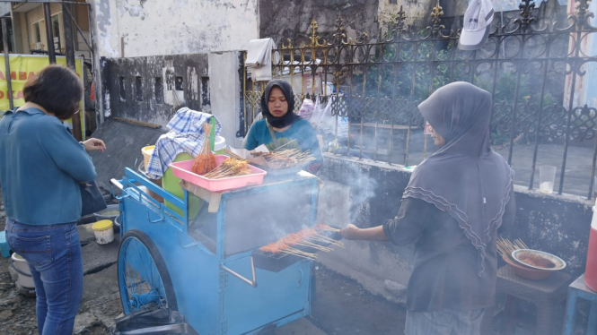 Tuminah, penjual sate klopo di Jalan Dinoyo saat melayani pembeli.