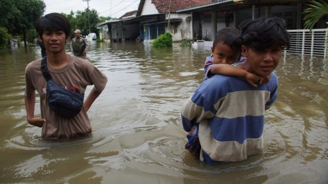 Warga melintasi jalan yang terendam banjir di Desa Jombok, Kecamatan Kesamben, Kabupaten Jombang.