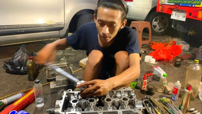 Fiki saat memperbaiki mesin mobil customer di bengkel miliknya.