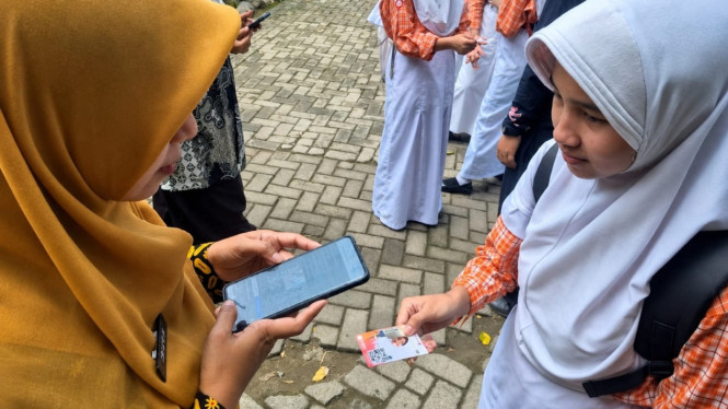 Seorang Guru Melakukan Presensi dengan scand barcode yang ada pada kartu pelajar.