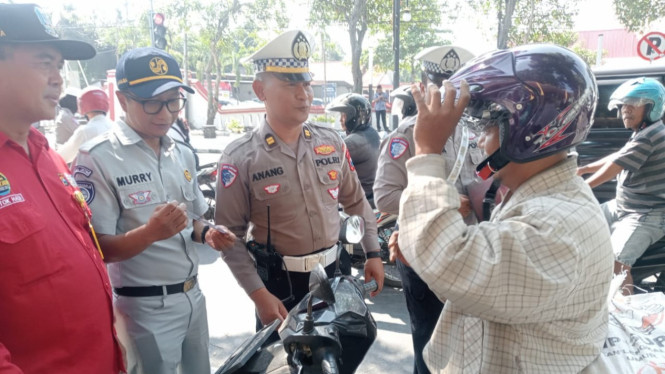 Polisi membagikan helm pada pengguna jalan raya.