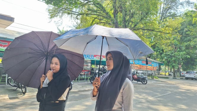 Dua wanita menggunakan payung melindungi diri cuaca panas di Kota Medan.