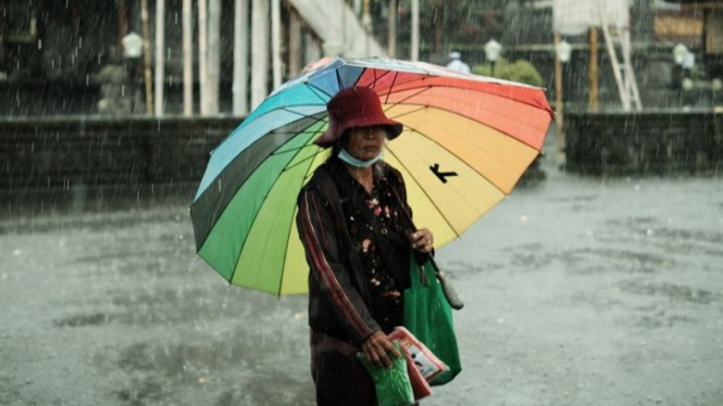 Ilustrasi sesorang memakai payung saat hujan.