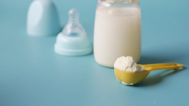 Botol susu yang berisi larutan putih yang belum tertutup dengan dot serta tutup disebelahnya