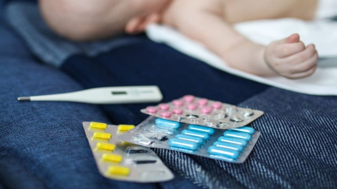 Seorang bayi terbaring di samping obat dan sebuah termometer