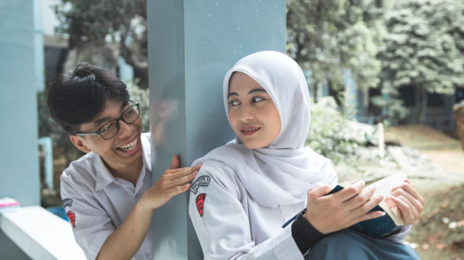 siswa SMA dan siswi SMA sedang duduk yang dipisahkan pilar di sekolah.