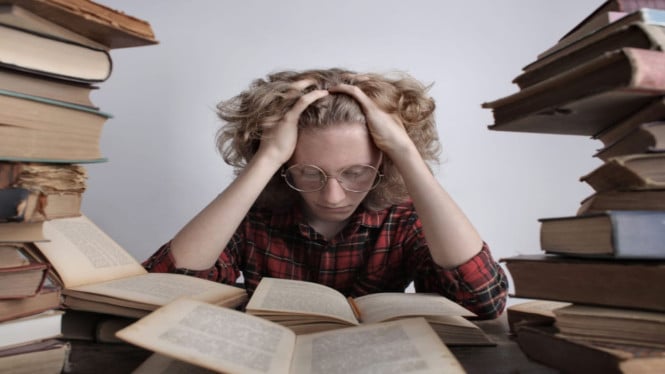 Remaja berkacamata yang stress dikelilingi tumpukan buku