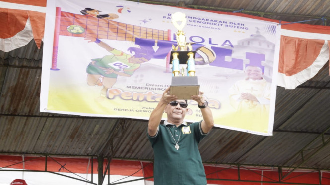 Pastor Paroki Santo Vitalis Cewonikit, RD Ardi Obot mengangkat piala bergilir yang akan diperebutkan dalam turnamen bola voli 2025 .