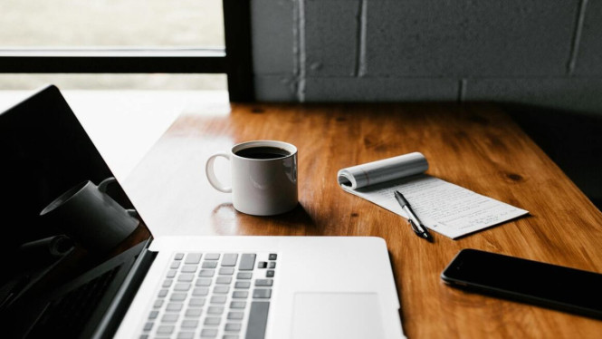 Segelas kopi di atas meja kayu cokelat dan Macbook Pro.
