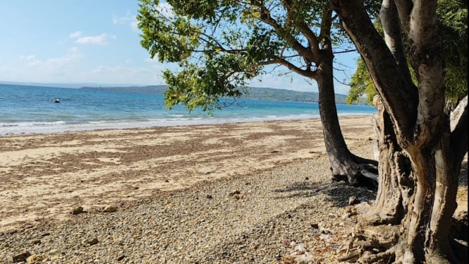 Keindahan pantai dengan laut biru dan pasir putih kecokelatan.